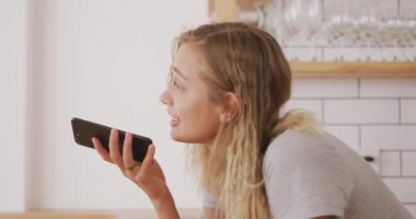 Beyaz kadın hafta sonları evde dinleniyor, mutfakta, masanın yanında oturuyor, akıllı telefonuyla konuşuyor. Karantina bölgesindeki sosyal mesafeler kilitlendi