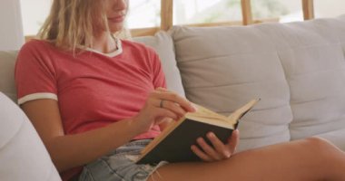 Beyaz kadın hafta sonları evde dinleniyor, kanepede oturuyor, kitap okuyor. Karantina bölgesindeki sosyal mesafeler kilitlendi