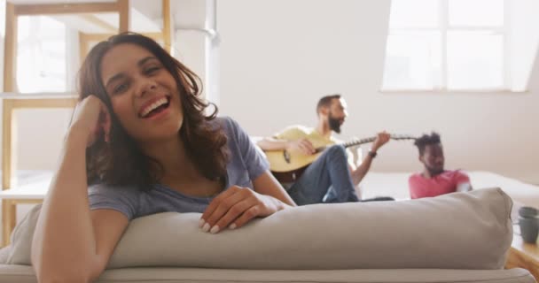 一个高加索女人的画像 周末在家里放松 看着相机 她的朋友们在后台弹奏吉他 — 图库视频影像