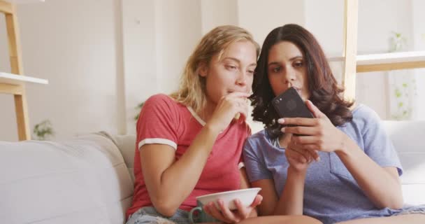 Two Caucasian Women Relaxing Home Weekend Sitting Sofa Eating Snacks — Stock Video