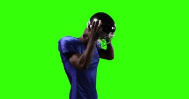 Kendine güvenen Afro-Amerikan futbolcu spor kıyafetleri giyiyor, yeşil ekran arka planına kask takıyor. Sporcu gücü.