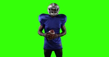 Spor kıyafetleri ve miğfer takmış, yeşil ekran arka planında kameraya bakan kendine güvenen Afro-Amerikan futbolcu portresi. Sporcu gücü.