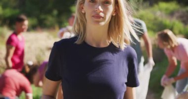 Kırsal kesimde güneşli bir günde nehri temizleyen bir grup koruma gönüllüsüyle birlikte çöp toplayan beyaz bir kadının portresi. Kırsal bir ortamda ekoloji ve sosyal sorumluluk.