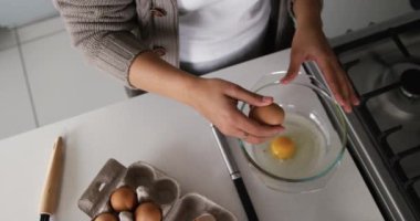Karışık ırktan bir kadının orta açı görüntüsü evde eğleniyor, kahvaltıyı mutfakta hazırlıyor, yumurtaları kaseye kırıyor, ağır çekim.