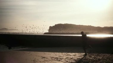 Afrika kökenli Amerikalı bir adam spor kıyafetleri giyiyor, güneşli bir günde egzersiz yapıyor, kumsalda koşuyor, duvarın önünden geçiyor.