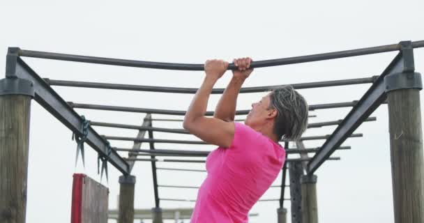 Rear view close up of a mixed-race woman wearing a pink t shirt exercising at boot camp, doing pull ups hanging from monkey bars, in slow motion — Stock Footage Rear View Close Mixed Race Woman Wearing Pink Shirt Exercising Royalty Free Stock Video