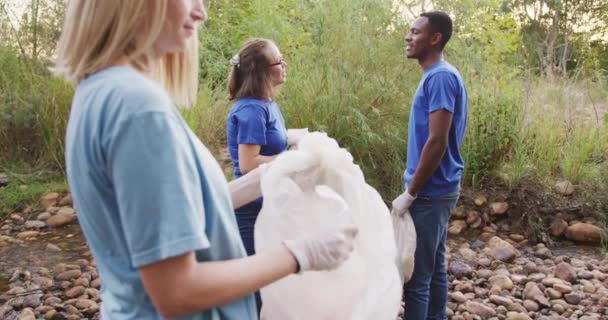 在一个阳光明媚的乡村 一群多种族的快乐的环保志愿者正在清理一条河 捡垃圾 农村环境中的生态和社会责任 — 图库视频影像