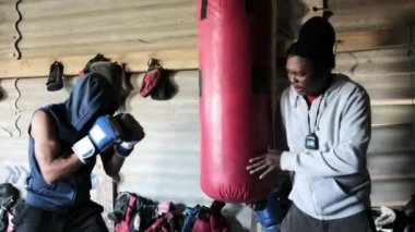 Afro-Amerikan erkek boksör boks eldiveni takıyor, boks antrenmanında eğitim görüyor. Afrika kökenli Amerikalı erkek antrenörünün tuttuğu kum torbasına yumruk atıyor.