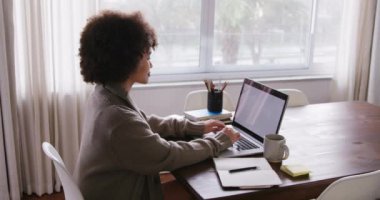 Karışık ırktan bir kadının evde vakit geçirmesinin yüksek açılı görüntüsü. Ev ofisteki bir masada oturup dizüstü bilgisayarda yazı yazması. Ağır çekimde.