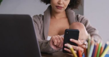 Karışık ırktan bir kadının evde vakit geçirmesinin ön görüntüsü, akıllı telefon ve dizüstü bilgisayar kullanarak, yavaş çekim