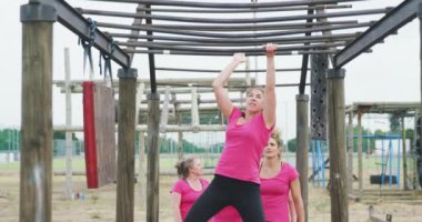 Acemi birliğinde egzersiz yapmaktan zevk alan beyaz bir kadının ön görüntüsü, diğer kadınlarla birlikte maymun parmaklıklarına tırmanmak, sıralarını beklemek ve arka planda yavaşça tezahürat yapmak.