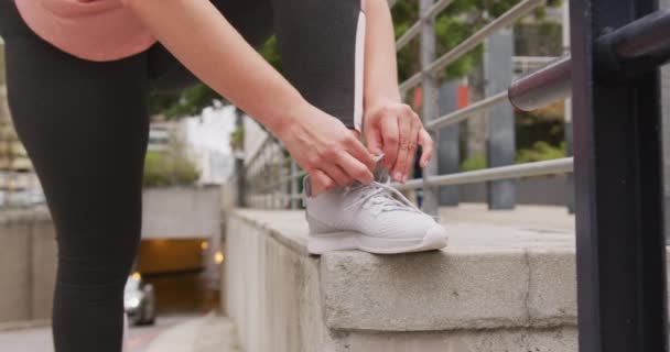 在城市里 身材低矮 一头乌黑长发 身穿运动服的高加索女人身穿运动服 腿上的鞋带靠在墙上 动作缓慢 — 图库视频影像