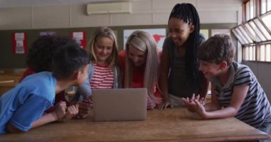 Okulda öğretmenleriyle birlikte dizüstü bilgisayar kullanan çok ırklı bir grup çocuk. Covid19 Coronavirus salgını sırasında temel eğitim sosyal güvenlikten uzaklaşma yavaş çekimde.