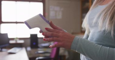 Okulda termometre tutan yüz maskesi takan bir bayan öğretmen. Covid19 Coronavirus salgını sırasında temel eğitim sosyal güvenlikten uzaklaşma yavaş çekimde.