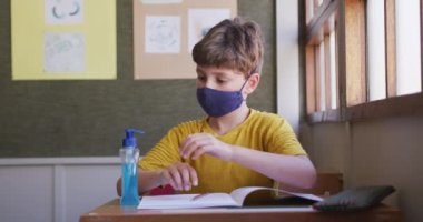Beyaz çocuk el dezenfektanı kullanıyor, okulda maske takıyor. Covid19 Coronavirus salgını sırasında temel eğitim sosyal güvenlikten uzaklaşma yavaş çekimde.