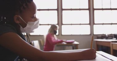Okulda maskesini takmış, kitap yazan melez bir kız. Covid19 Coronavirus salgını sırasında temel eğitim sosyal güvenlikten uzaklaşma yavaş çekimde.