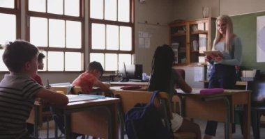 Okulun sınıfında bir grup çok ırklı çocuk var. Öğretmen tabletini kullanıyor. Covid19 Coronavirus salgını sırasında temel eğitim sosyal güvenlikten uzaklaşma yavaş çekimde.
