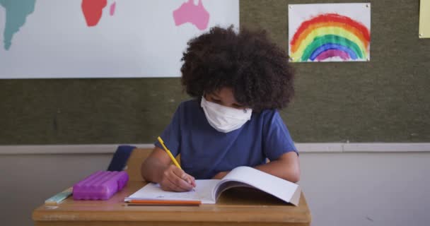 Chica Raza Mixta Escribiendo Libro Usando Mascarilla Mientras Está Sentada — Vídeo de stock