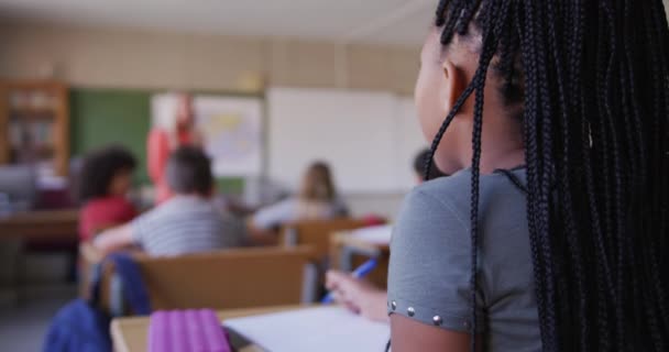 学校の机の上に座っている間に 授業に焦点を当てた複雑なレースの女の子は笑っていました Covid19時の初等教育社会的距離の健康上の安全性スローモーションでコロナウイルスパンデミック — ストック動画