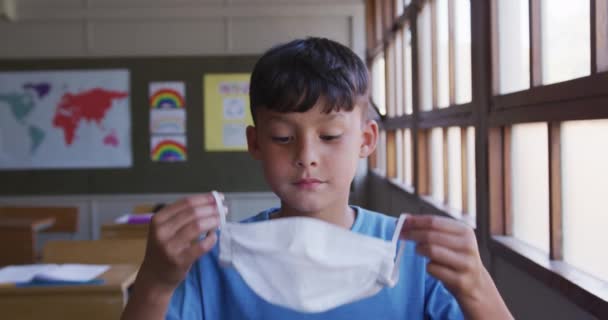 Niño Caucásico Poniéndose Una Mascarilla Sentado Escritorio Escuela Mirando Cámara — Vídeo de stock