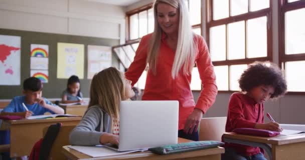 学校の机の上に座っている間 ノートパソコンを使っている白人の女の子 彼女を助ける彼女の先生 Covid19時の初等教育社会的距離の健康上の安全性スローモーションでコロナウイルスパンデミック — ストック動画