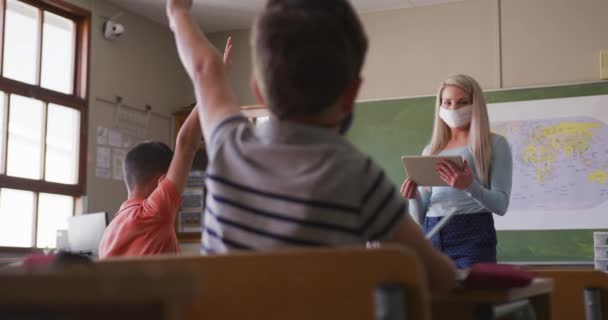 女教师戴着面罩 用平板电脑指着学校的一名学生 Covid19 Coronavirus流感大流行期间 初等教育在社会上与健康安全保持距离的慢动作 — 图库视频影像