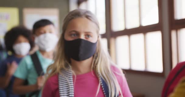 学校の教室でキューに立って顔のマスクを身に着けている子供たちのグループ Covid19時の初等教育社会的距離の健康上の安全性スローモーションでコロナウイルスパンデミック — ストック動画
