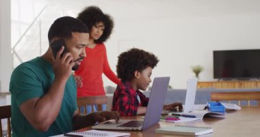 Karışık ırk çifti ve oğlu evde birlikte vakit geçiriyorlar, sosyal mesafeler ve karantina altında kendilerini izole ediyorlar, baba ve oğul dizüstü bilgisayar kullanıyorlar, ağır çekimde.