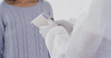 Karışık ırk kadın sosyal mesafesi ve karantinada kendini izole etme, yüz maskesi takmak, koruyucu giysiler giyen biri tarafından vücut ısısını ölçmek, yavaş çekim