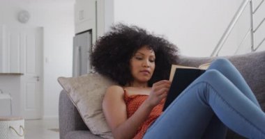 Karışık ırk kadın sosyal mesafesi ve karantina tecridi, kanepede uzanıp kitap okumak, yavaş çekim.