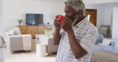 Afrika kökenli Amerikalı son sınıf öğrencisi bir fincan kahve içiyor, pencereden bakıyor, sosyal mesafeler ve karantina tecridinde kendini izole etme, yavaş çekim.