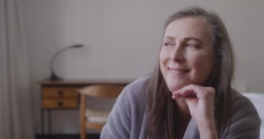 Kafkasyalı mutlu bir kadının evde vakit geçirmesini, sosyal mesafeyi ve kendini karantinaya almasını, yatak odasında oturmasını, ağır çekimde gülümsemesini..