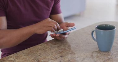 Evde melez bir ırk, sosyal mesafeler ve karantina tecridi, bir masada oturup akıllı telefonunu peçeteyle temizleme, yavaş çekim.