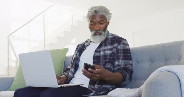 非裔美国老人坐在沙发上 用笔记本电脑和智能手机 在隔离 慢动作中保持社交距离和自我隔离 — 图库视频影像