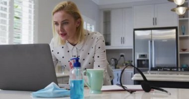 Beyaz kadın evde vakit geçiriyor, laptopta sohbet ediyor mutfakta yavaş çekimde. Covid 19 Coronavirus karantina süresince sosyal mesafeler.
