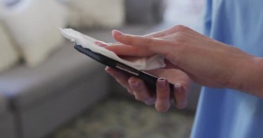 Beyaz kadın hemşire, akıllı telefonu mendille temizliyor. Covid 19 Coronavirus karantinası sırasında evde tıbbi bakım, yavaş çekim.