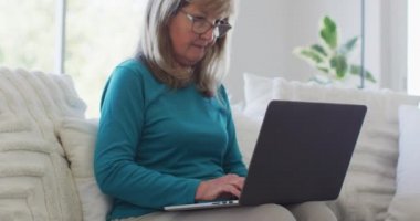 Üst düzey beyaz kadın evinde oturuyor, oturma odasında dizüstü bilgisayar kullanıyor. Covid 19 Coronavirus karantina süresince sosyal mesafeler