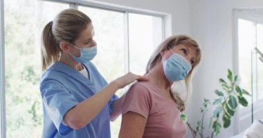 Kafkas kadın hemşire tarafından ziyaret edilmiş, boynunu uzatmış, maske takmış hemşire. Covid 19 Coronavirus karantinası sırasında evde tıbbi bakım, yavaş çekim
