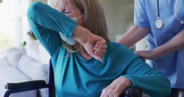 Beyaz kadın hemşire tarafından ziyaret edilmiş, öksürürken ağzını kapamış, maske takmış bir hemşire. Covid 19 Coronavirus karantinası sırasında evde tıbbi bakım, yavaş çekim.