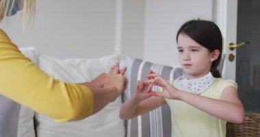 Beyaz kadın kızıyla birlikte evde vakit geçiriyor, yüz maskeleriyle kanepede yavaş çekimde işaret dili kullanıyor. Covid 19 Coronavirus karantina süresince sosyal mesafeler.