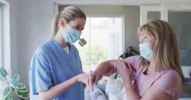 Beyaz kadın hemşire tarafından ziyaret edilmiş, dirseğini uzatmış, maske takmış hemşire. Covid 19 Coronavirus karantinası sırasında evde tıbbi bakım, yavaş çekim