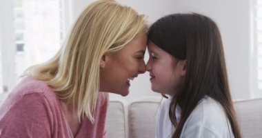 Beyaz bir kadın kızıyla birlikte evde vakit geçiriyor, yavaş çekimde gülümsüyor. Covid 19 Coronavirus karantina süresince sosyal mesafeler.