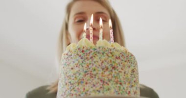 Beyaz kadın evde vakit geçiriyor, mutfakta doğum günü pastasıyla oturuyor. Covid 19 Coronavirus karantinası sırasındaki sosyal mesafeler, yavaş çekim.