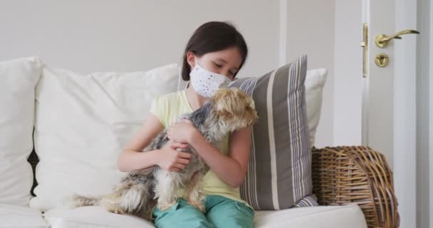 白人女孩穿着面具呆在家里 抱着宠物狗坐在沙发上 动作缓慢 Covid期间的社会疏离 — 图库视频影像