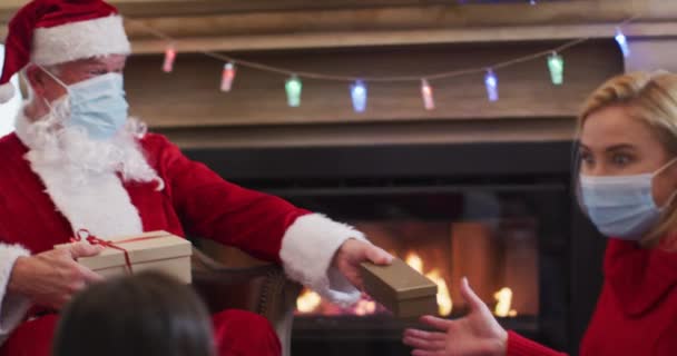 サンタクロースはフェイスマスクを着用し 母と娘へのギフトボックスを自宅でクリスマスにフェイスマスクで スローモーションで与えます Covid 19コロナウイルス隔離ロックダウン中の社会的距離 — ストック動画