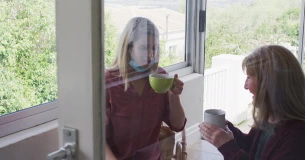 シニア白人女性は大人の娘と一緒に家で時間を過ごし ソファに座ってお茶を飲んでいます Covid 19コロナウイルス隔離中の社会的距離 スローモーション — ストック動画
