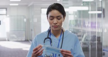 Melez kadın tıp uzmanının portresi. Yüzüne maske takıyor ve boynuna steteskopla kameraya bakıyor. Coronavirus Covid 19 salgını sırasında işyerinde hijyen..