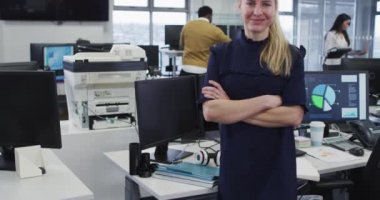 Sıradan bir ofiste çalışan beyaz bir kadın, bilgisayarlı bir masada ağır çekimde oturuyor, kameraya bakıyor ve gülümsüyor. Coronavirus Covid 19 salgını sırasında işyerinde sosyal mesafeler.