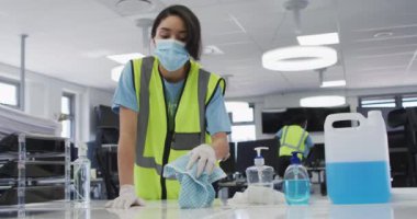 Ofisi temizleyen, çelik yelek, eldiven ve yüz maskesi takan, dezenfektan kullanan, arka planda çalışan, ağır çekim yapan melez bir kadın. Coronavirus Covid 19 salgını sırasında işyerinde hijyen