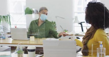 Ofis maskesinde koruyucu ekranlarla çalışan maskeli kadın ve erkek karışık yarış maskeleri, erkek belgesi veren kadın, ağır çekim. Coronavirus Covid 19 salgını sırasında işyerinde sağlık ve hijyen.